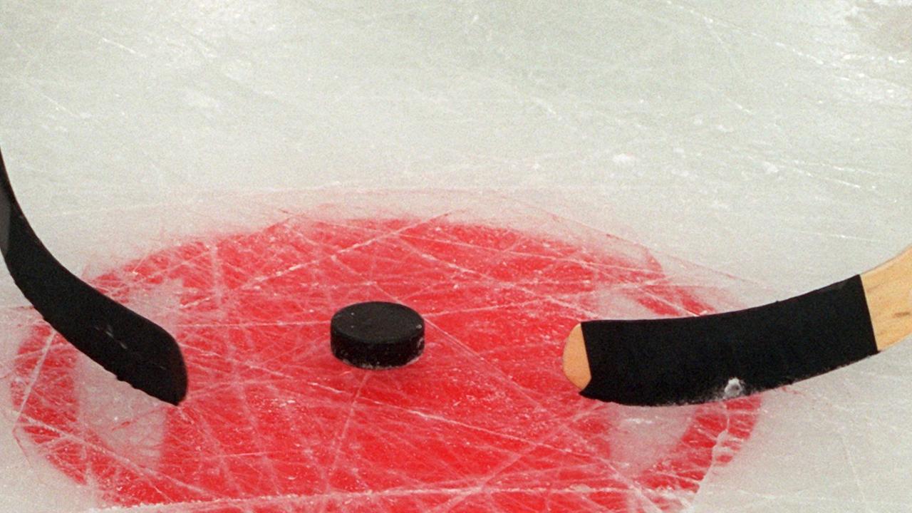 Zwei Eishockeyschläger liegen an einem Puck Zwei Eishockeyschläger liegen an einem Puck