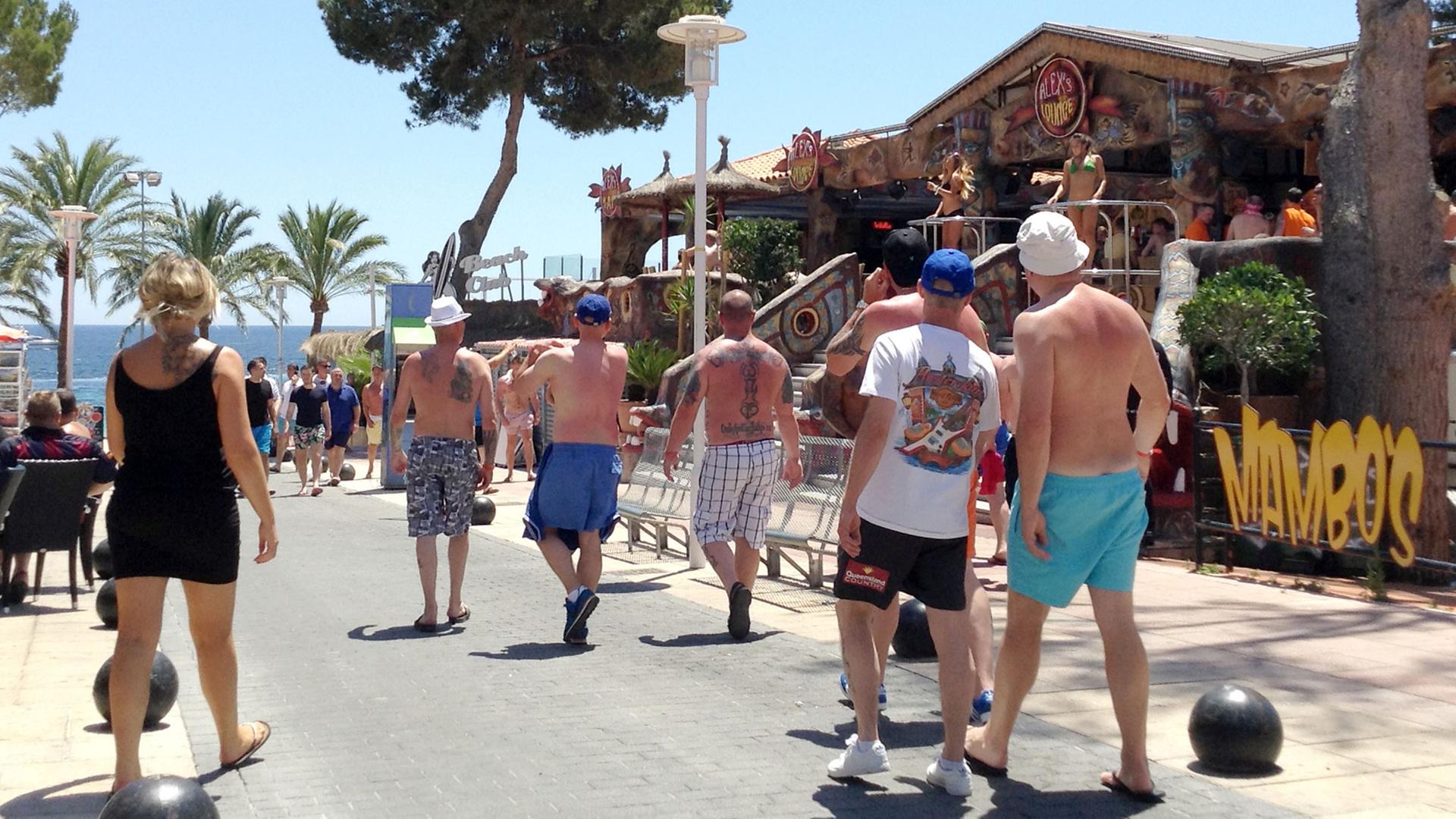 Touristen schlendern am 06.06.2015 durch eine Straße in Magaluf, Mallorca, während leicht bekleidete Tänzerinnen in einem Lokal schon mittags die Stimmung anheizen. Touristen schlendern am 06.06.2015 durch eine Straße in Magaluf, Mallorca, während leicht bekleidete Tänzerinnen in einem Lokal schon mittags die Stimmung anheizen.