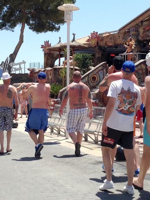 Touristen schlendern am 06.06.2015 durch eine Straße in Magaluf, Mallorca, während leicht bekleidete Tänzerinnen in einem Lokal schon mittags die Stimmung anheizen.
