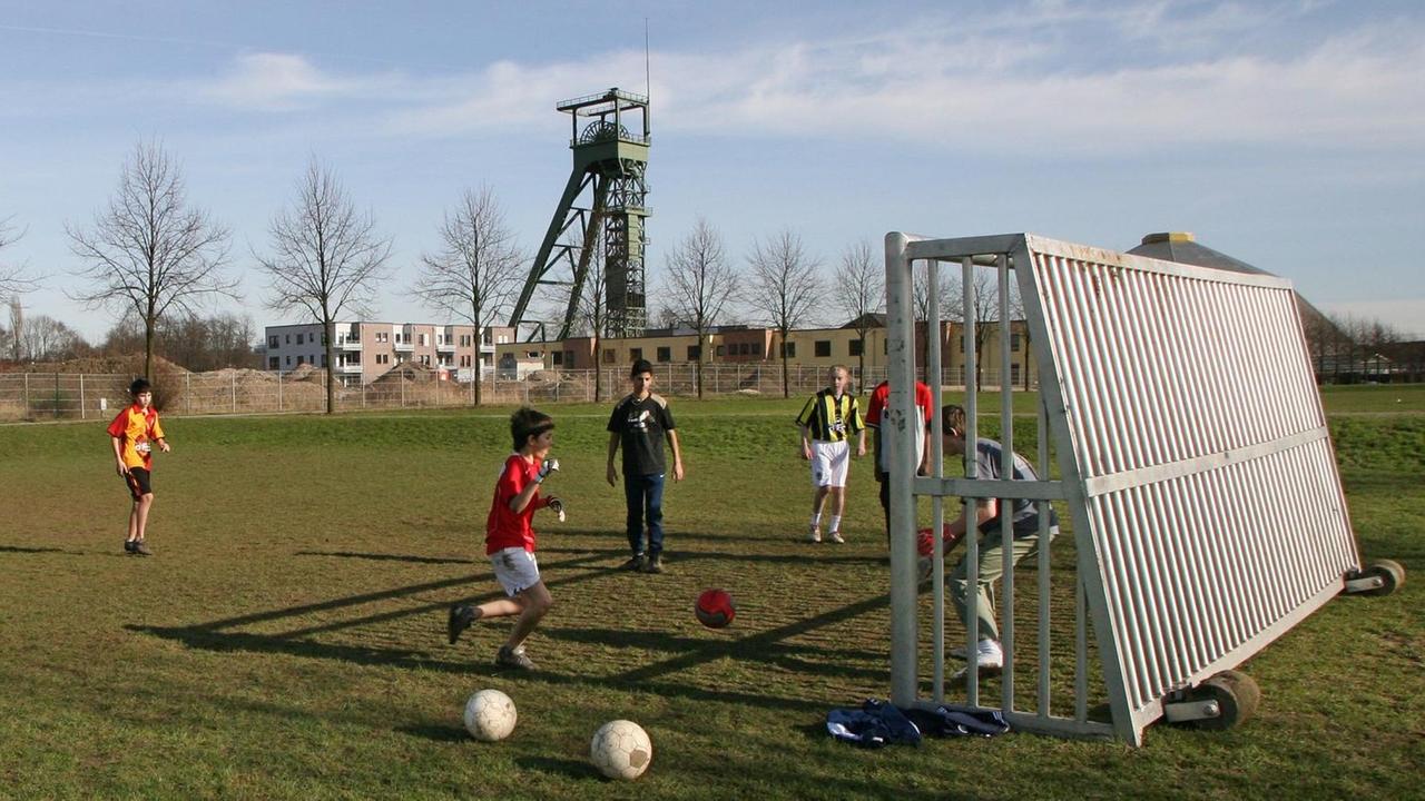 Kinder spielen auf einem Sportplatz vor dem alten Förderturm der Zeche Osterfeld in Oberhausen Fußball (Foto vom 16.02.2007). Die Jugendlichen treten vor einem Industriedenkmal gegen die Lederkugel.