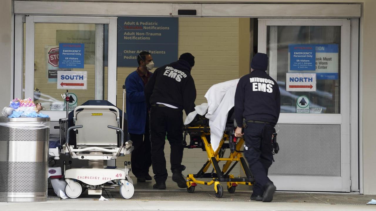 Zwei Männer bringen einen Kranken auf einer fahrbaren Liege in ein Krankenhaus in New York.