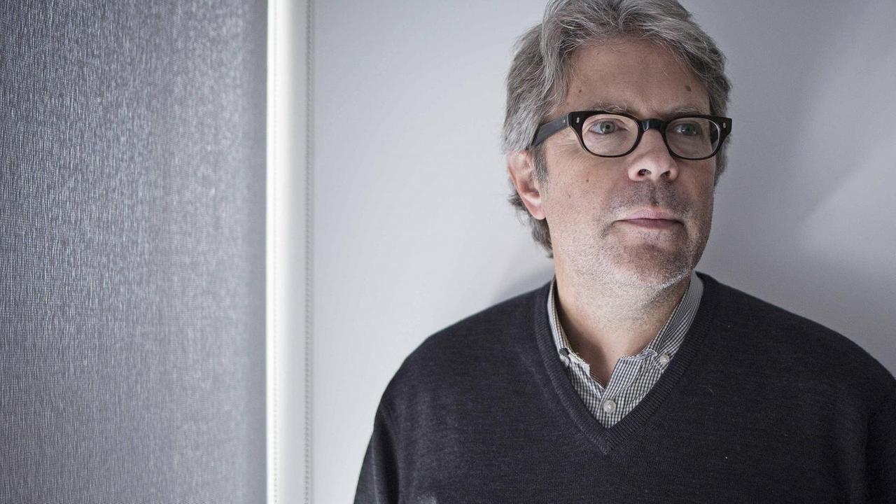 Jonathan Franzen trägt einen blauen Pullover und steht mit ernstem Blick vor einer weißgrauen Wand. Jonathan Franzen trägt einen blauen Pullover und steht mit ernstem Blick vor einer weißgrauen Wand.