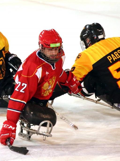 Spielszene auf dem Eis zwischen 2 deutschen und einem russischen Para-Eishockey-Athleten.