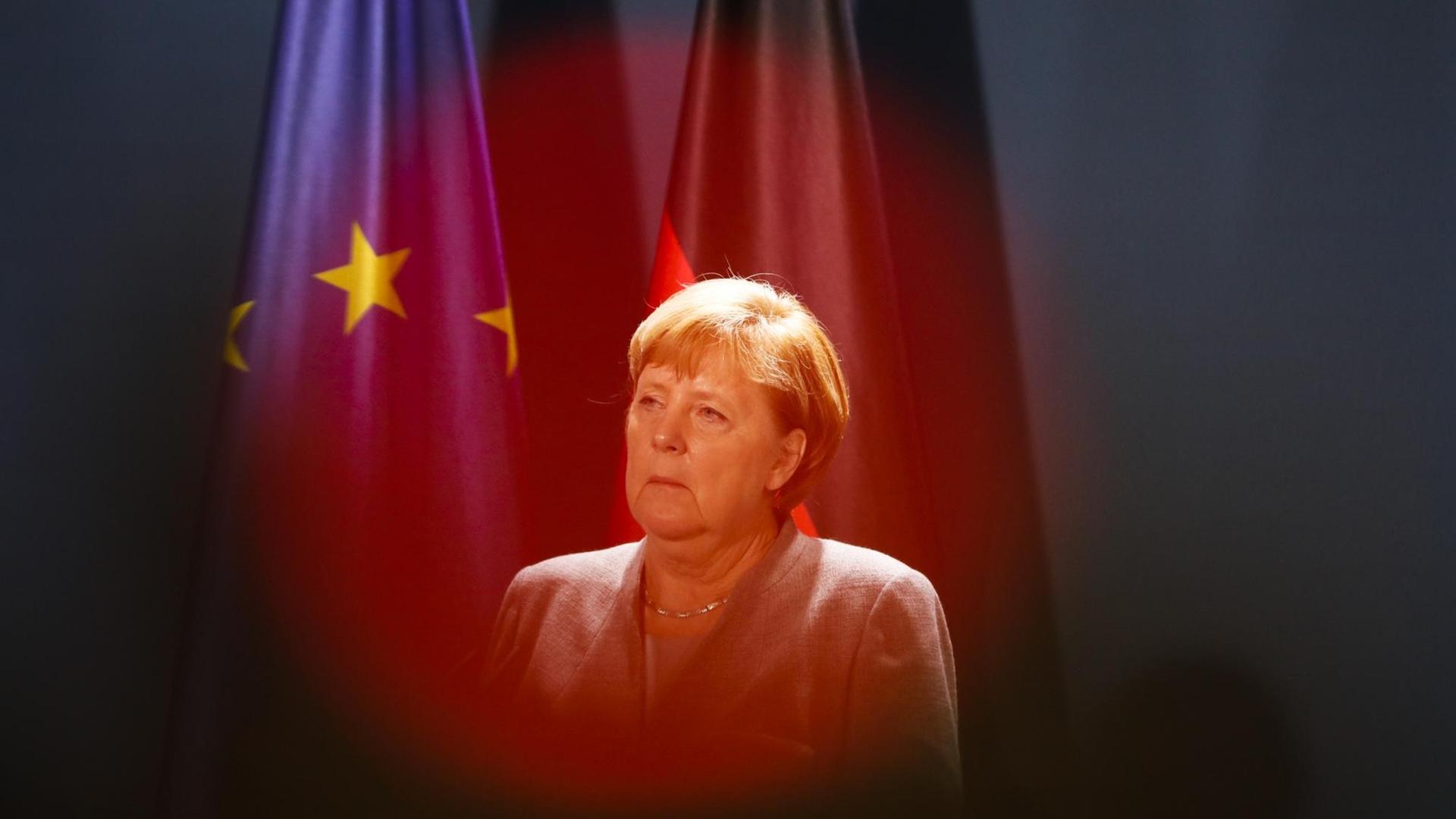 Das Rotlicht einer Fernsehkamera liegt auf Bundeskanzlerin Angela Merkel (CDU), die vor einer Deutschland- und einer EU-Flagge zu sehen ist.