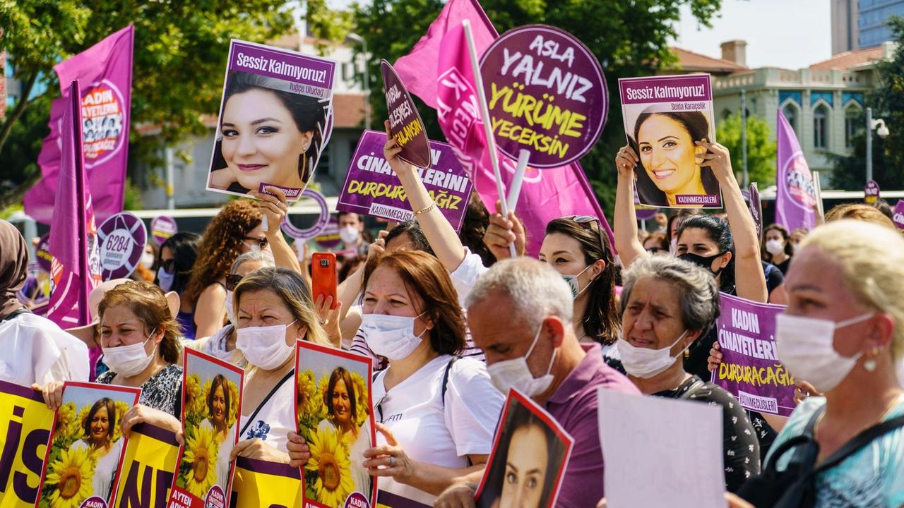 Viele dicht beieinander stehende Menschen mit Mundschutz demonstrieren mit lila Plakaten und rosa Fahnen sowie mit Fotos getöteter Frauen gegen Gewalt gegen Frauen. Viele dicht beieinander stehende Menschen mit Mundschutz demonstrieren mit lila Plakaten und rosa Fahnen sowie mit Fotos getöteter Frauen gegen Gewalt gegen Frauen.