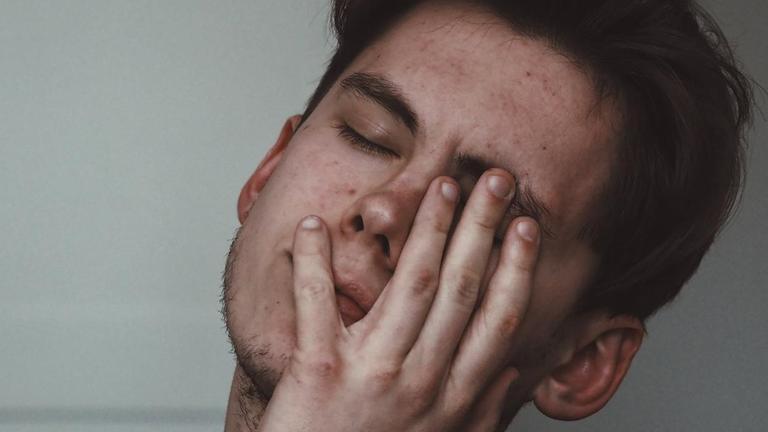 Ein erschöpfter junger Mann legt sein Gesicht mit geschlossenen Augen in seine Hand Ein erschöpfter junger Mann legt sein Gesicht mit geschlossenen Augen in seine Hand