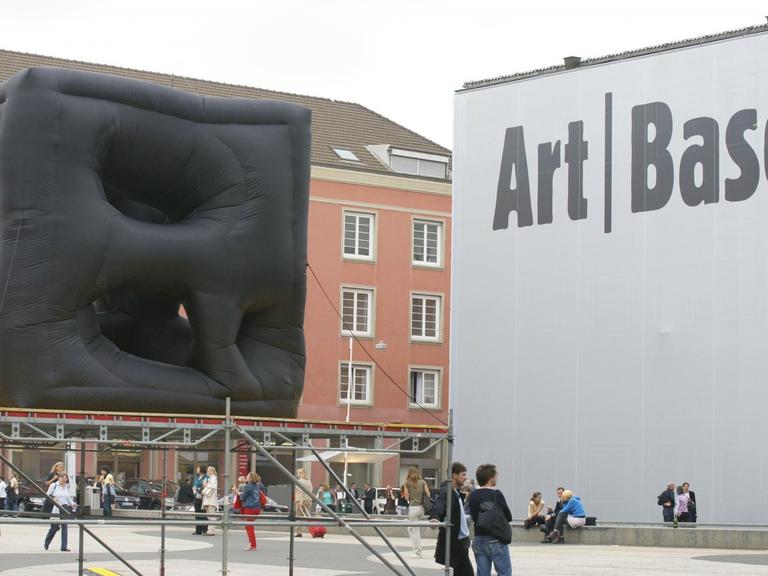 Vor der Messehalle der Art Basel steht eine große, schwarze, viereckige Skulptur. 