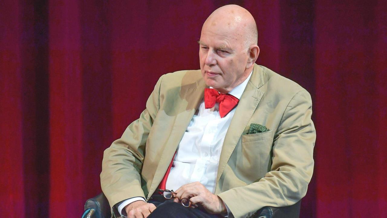 Ein älterer Mann sitzt auf einer Bühne. Ein älterer Mann sitzt auf einer Bühne.
