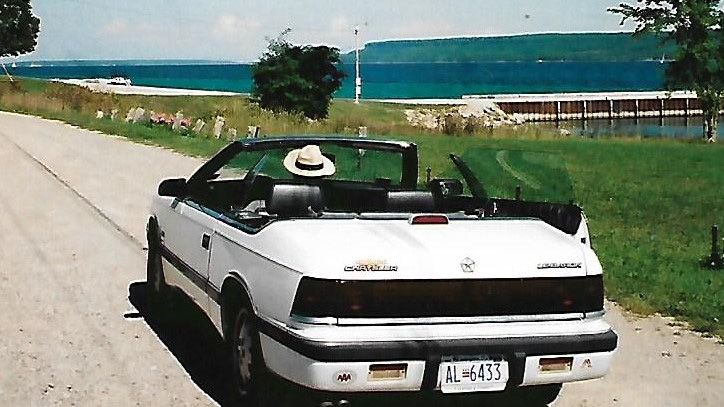 Günther Wessel mit seinem Chrysler Le Baron 1998. Ein weißes Cabrio fährt über eine Straße. Günther Wessel mit seinem Chrysler Le Baron 1998. Ein weißes Cabrio fährt über eine Straße.