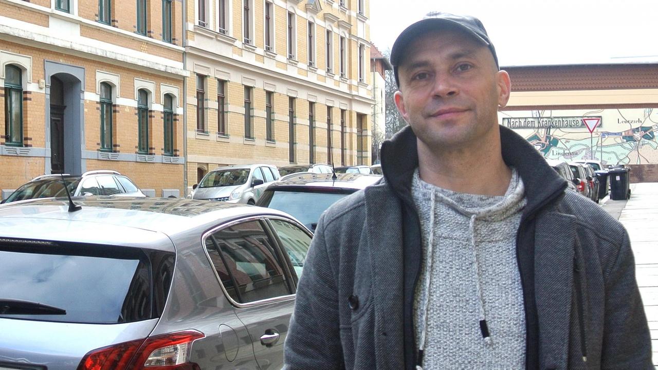 Ein Mann mit Basecap steht in einer Straße vor alten Mietshäusern und geparkten Autos. Ein Mann mit Basecap steht in einer Straße vor alten Mietshäusern und geparkten Autos.