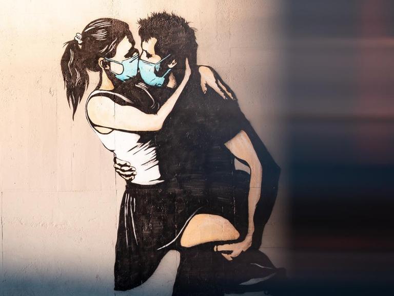 Street Art in Bryne, Norwegen. Auf einer Wand sieht man die Darstellung eines Pärchens, beide tragen medizinische Masken und sind im Begriff, sich zu küssen.