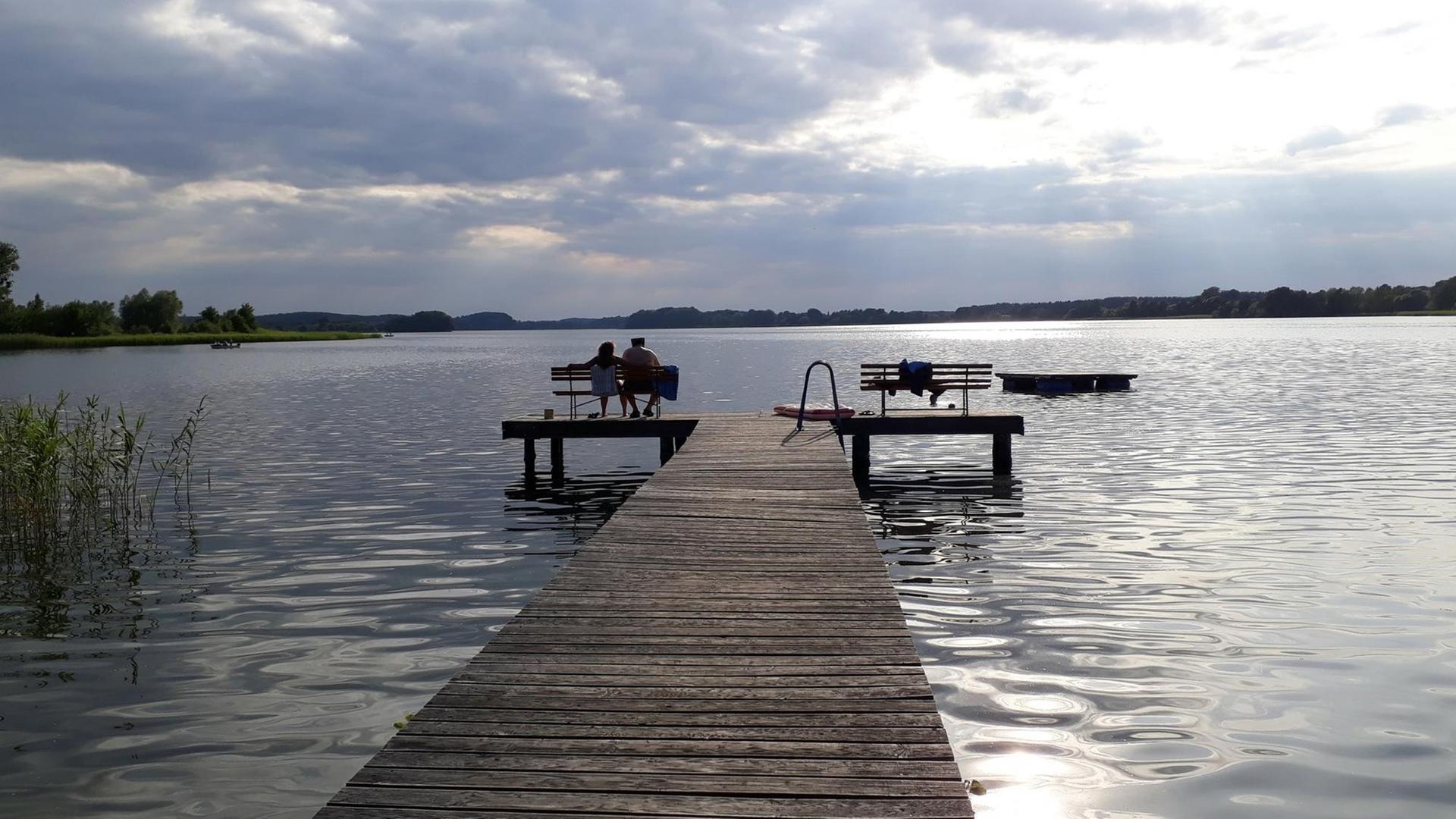 Menschen sitzen in der Sonne auf einem Steg am See von Serrahn. Menschen sitzen in der Sonne auf einem Steg am See von Serrahn.