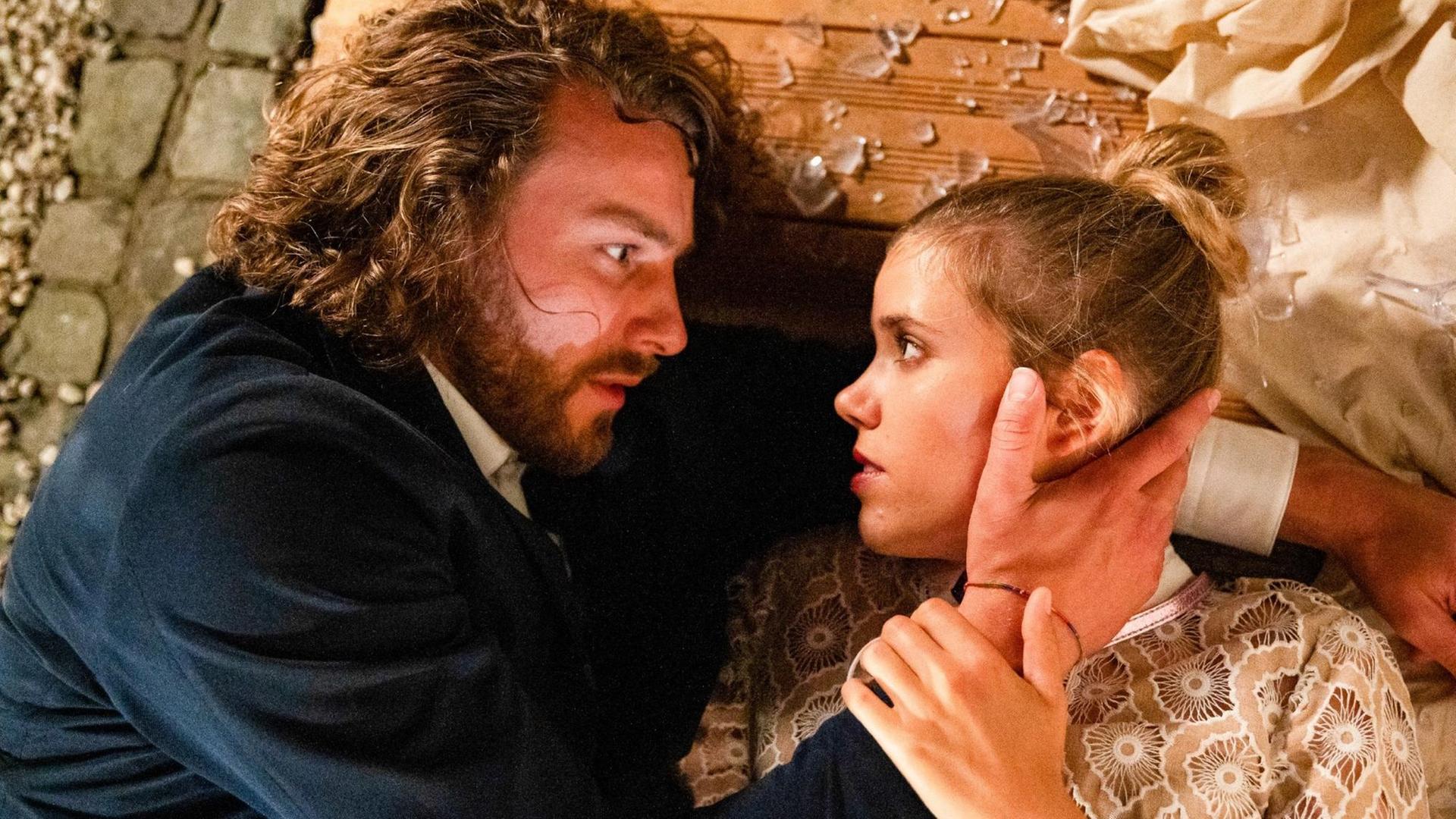 Alexander Verhoven und Josefin Reinhard liegen auf dem Boden und berühren sich inmitten von Glassplittern. Alexander Verhoven und Josefin Reinhard liegen auf dem Boden und berühren sich inmitten von Glassplittern.