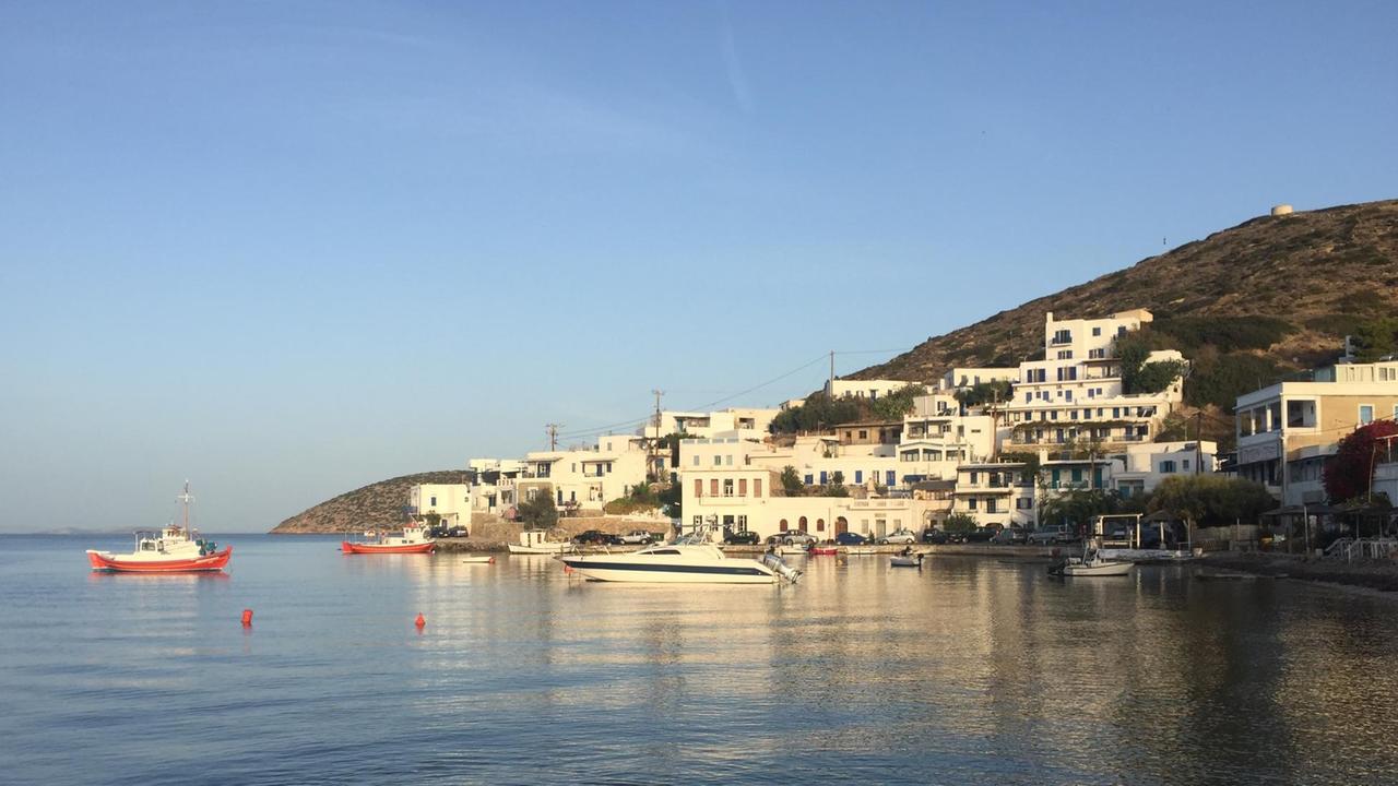 Der Hafen einer Insel mit weißen Häuschen am ruhigen glatten Meer mit blauem Himmel und Sonne.
