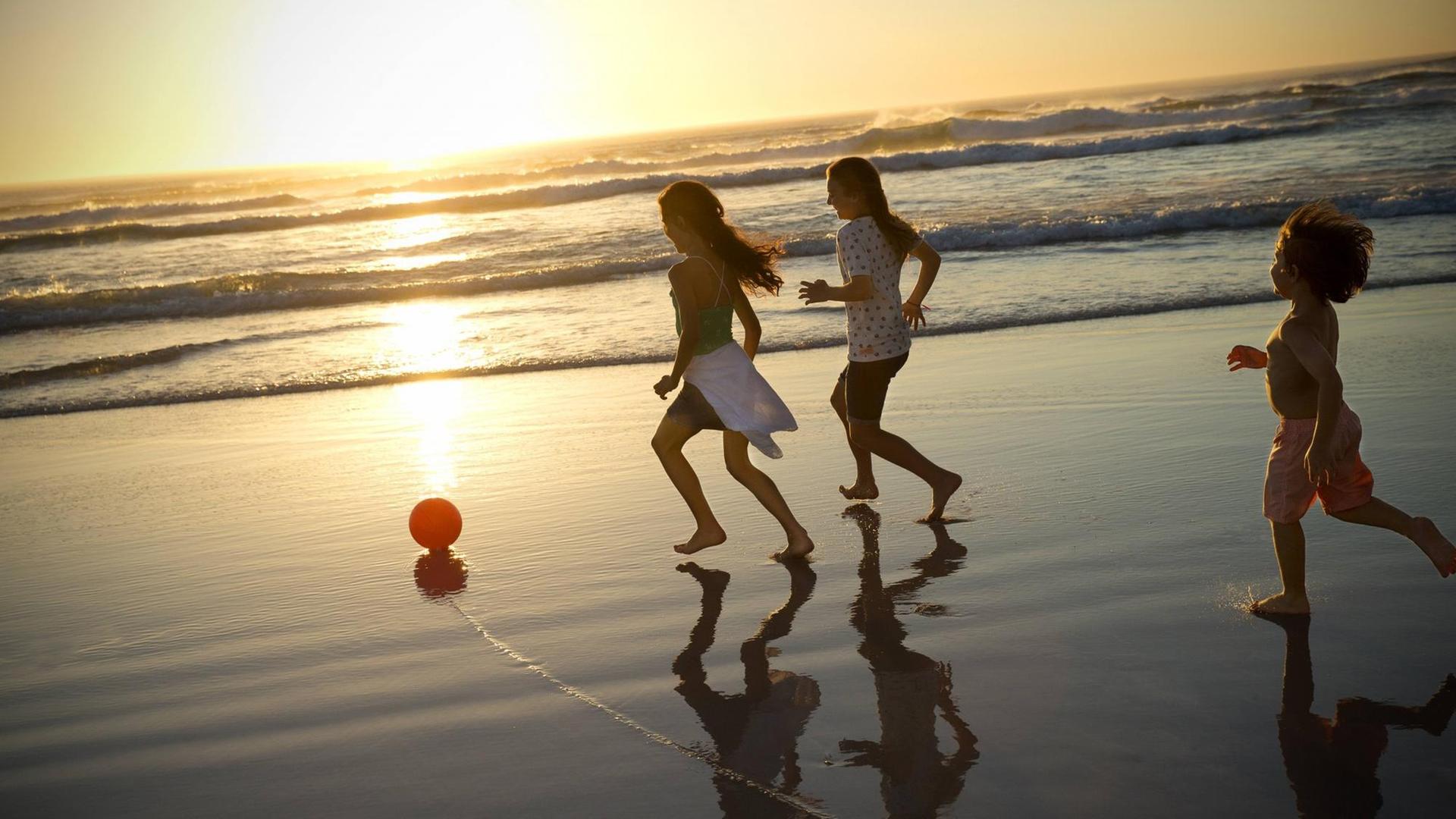 Kinder spielen am Strand im Sonnenuntergang mit einem Ball.