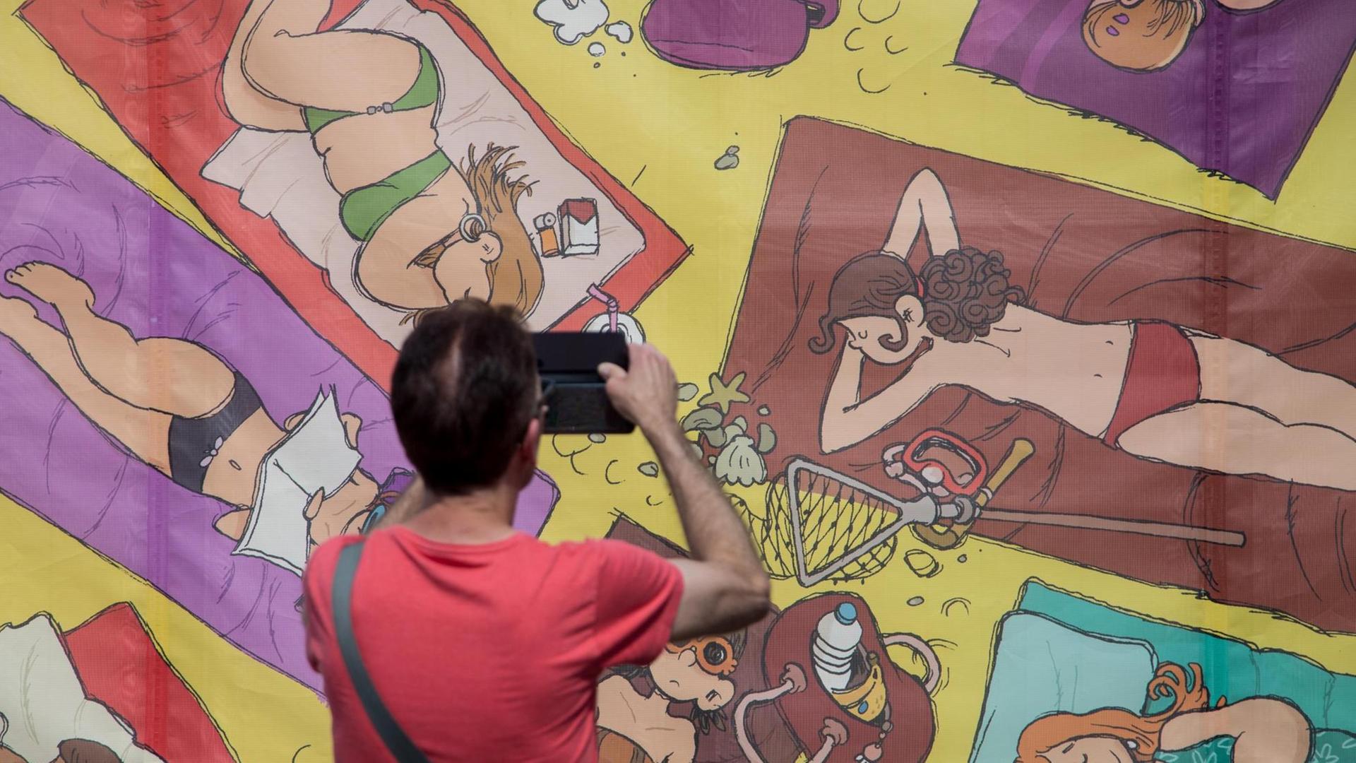 Eine Wand bemalt mit Comicfiguren, ein Mann fotografiert sie. Eine Wand bemalt mit Comicfiguren, ein Mann fotografiert sie.