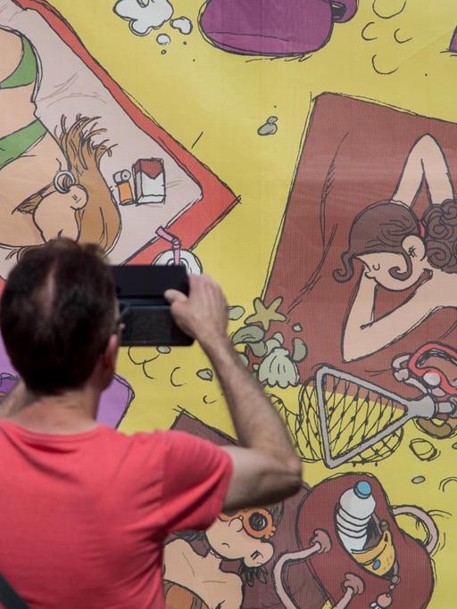 Eine Wand bemalt mit Comicfiguren, ein Mann fotografiert sie.