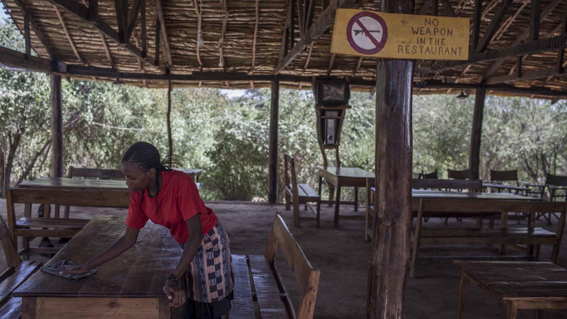 Eine Frau wischt in Kenia über den Tisch eines Restaurants. An einer Pfeiler ist ein Schild mit der Aufschrift "No Weapons in the Restaurant" angebracht. Eine Frau wischt in Kenia über den Tisch eines Restaurants. An einer Pfeiler ist ein Schild mit der Aufschrift "No Weapons in the Restaurant" angebracht.