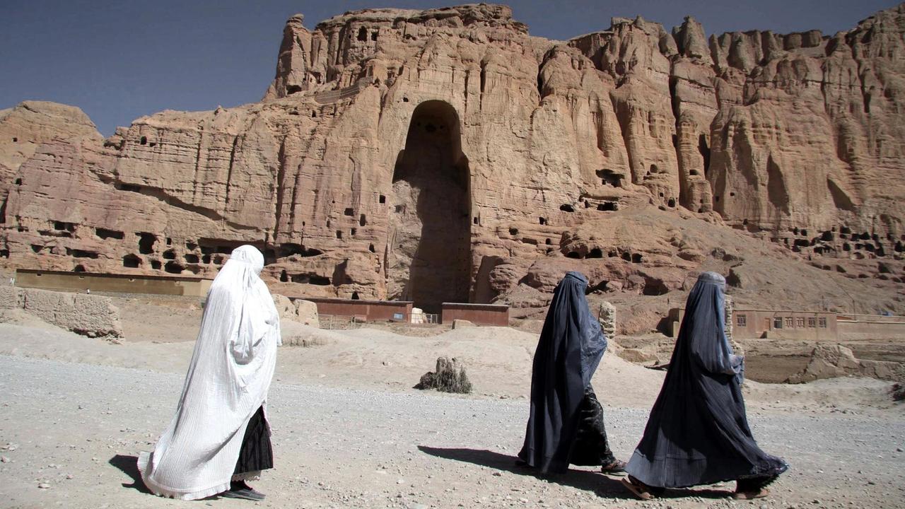 Afghanische Frauen laufen durch das Tal von Bamiyan. Im Hintergrund sieht man ein riesige Felsnische, wo die von den Taliban zerstörten Buddha-Statuen standen.