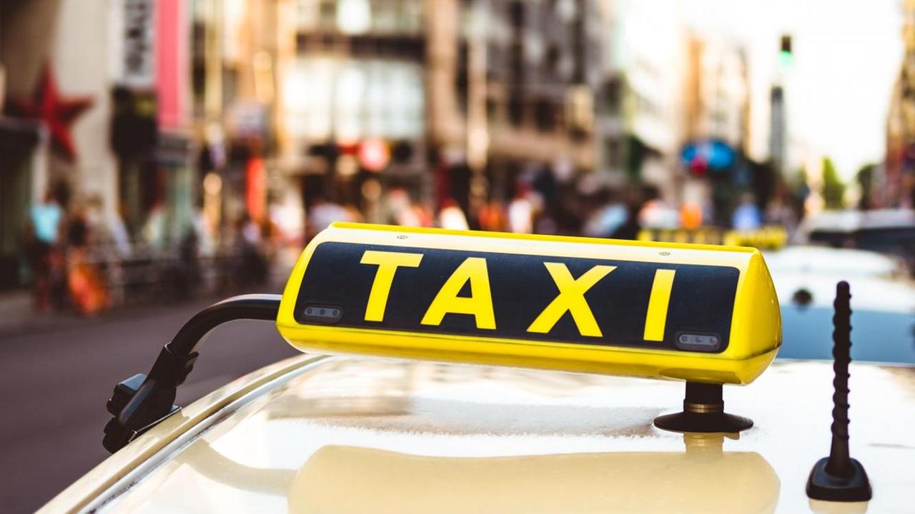 Ein Taxi im Zentrum von Berlin, im Vordergrund das Taxischild auf dem Dach des Autos, im Hintergrund eine Straße nahe des Checkpoint Charlie mit einem Eingang zur U-Bahn. Ein Taxi im Zentrum von Berlin, im Vordergrund das Taxischild auf dem Dach des Autos, im Hintergrund eine Straße nahe des Checkpoint Charlie mit einem Eingang zur U-Bahn.