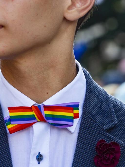Ein junger Mensch im Anzug mit einer Fliege in Regenbogenfarben.