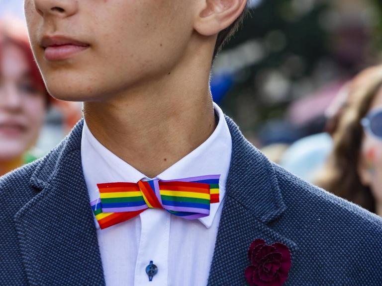 Ein junger Mensch im Anzug mit einer Fliege in Regenbogenfarben.