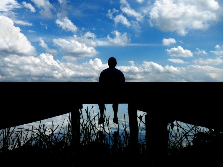 Ein Mann sitzt alleine auf einem Steg am See