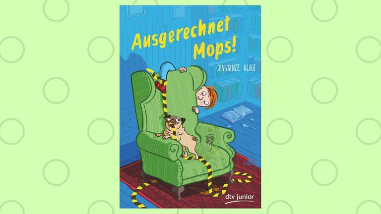 Constanze Klaue: "Ausgerechnet Mops"

Zu sehen ist das Buchcover: Ein Mops steht auf einem grünen Sessel, im Maul eine rot-schwarze Schnur, die um den Fuß eines Jungen geknotet ist. Der Junge schaut hinter dem Sessel hervor und das eine Bein hängt über die Sessellehne