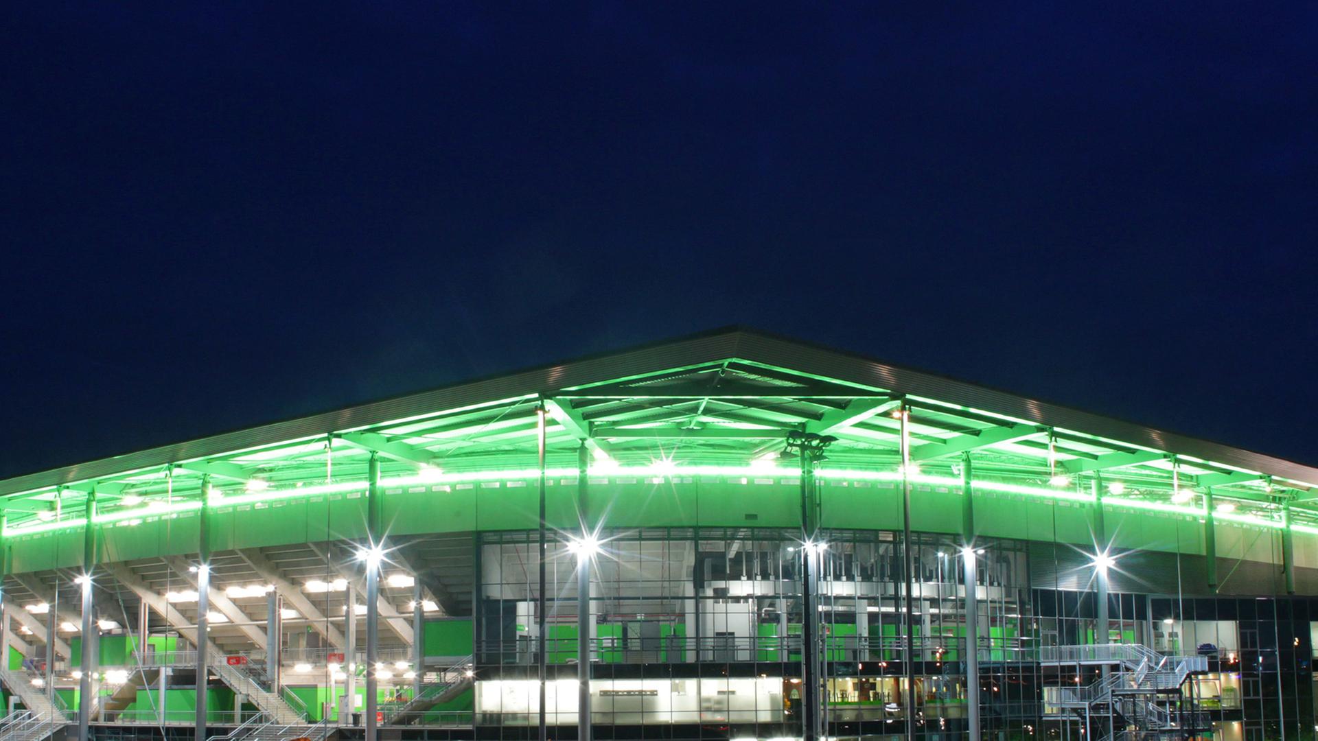 Die Teilansicht des Wolfsburger Stadions zeigt eine Ecke des mehrstöckigen Gebäudes, dessen überhängendes Dach grün angestrahlt ist.