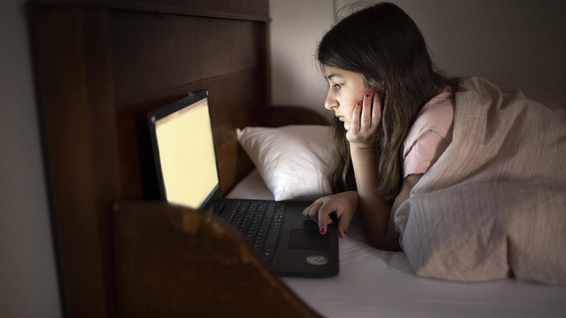Ein Mädchen an ihrem Laptop, nachts in ihrem Bett. (Symbolbild)