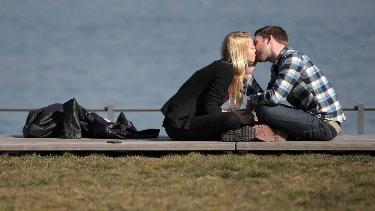 Ein verliebtes Paar genießt in Mainz am Rheinufer das sonnige Wetter und küssen sich auf der Uferpromenade.