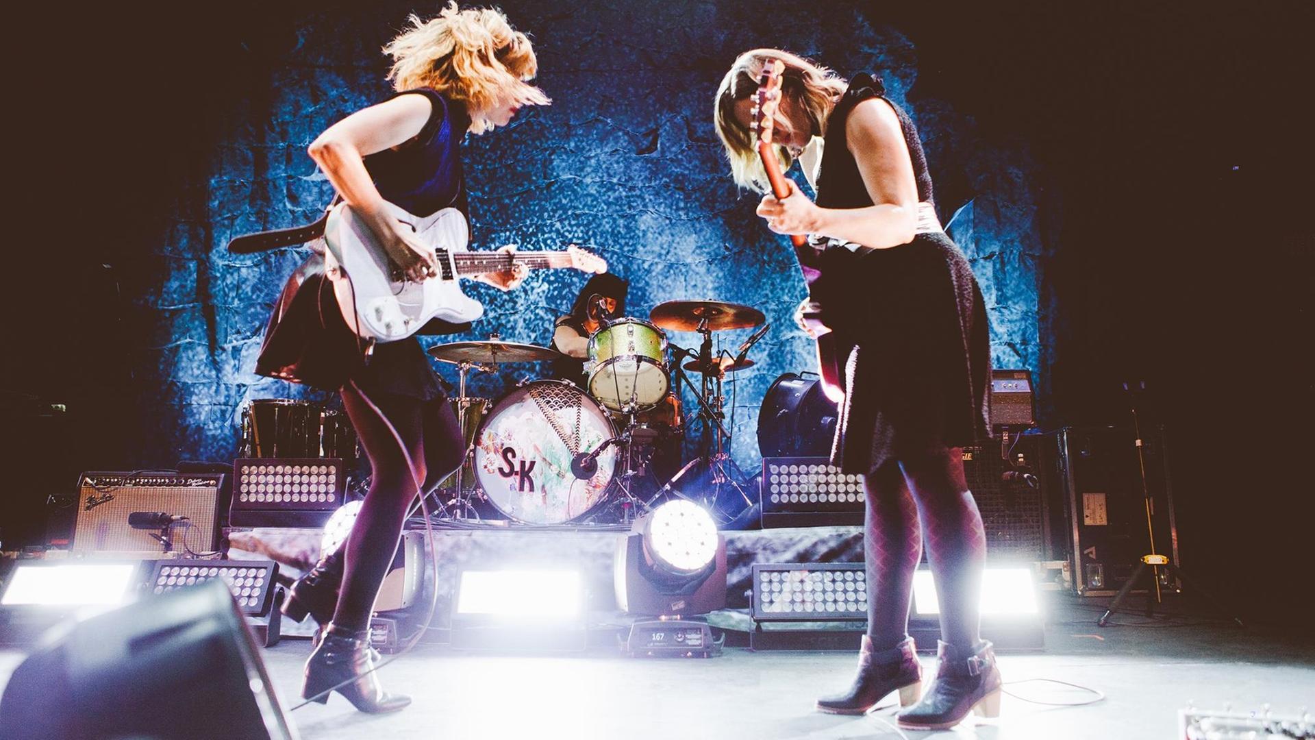 Sleater Kinney spielen auf der Bühne mit zwei Gitarren und Schlagzeug Sleater Kinney spielen auf der Bühne mit zwei Gitarren und Schlagzeug