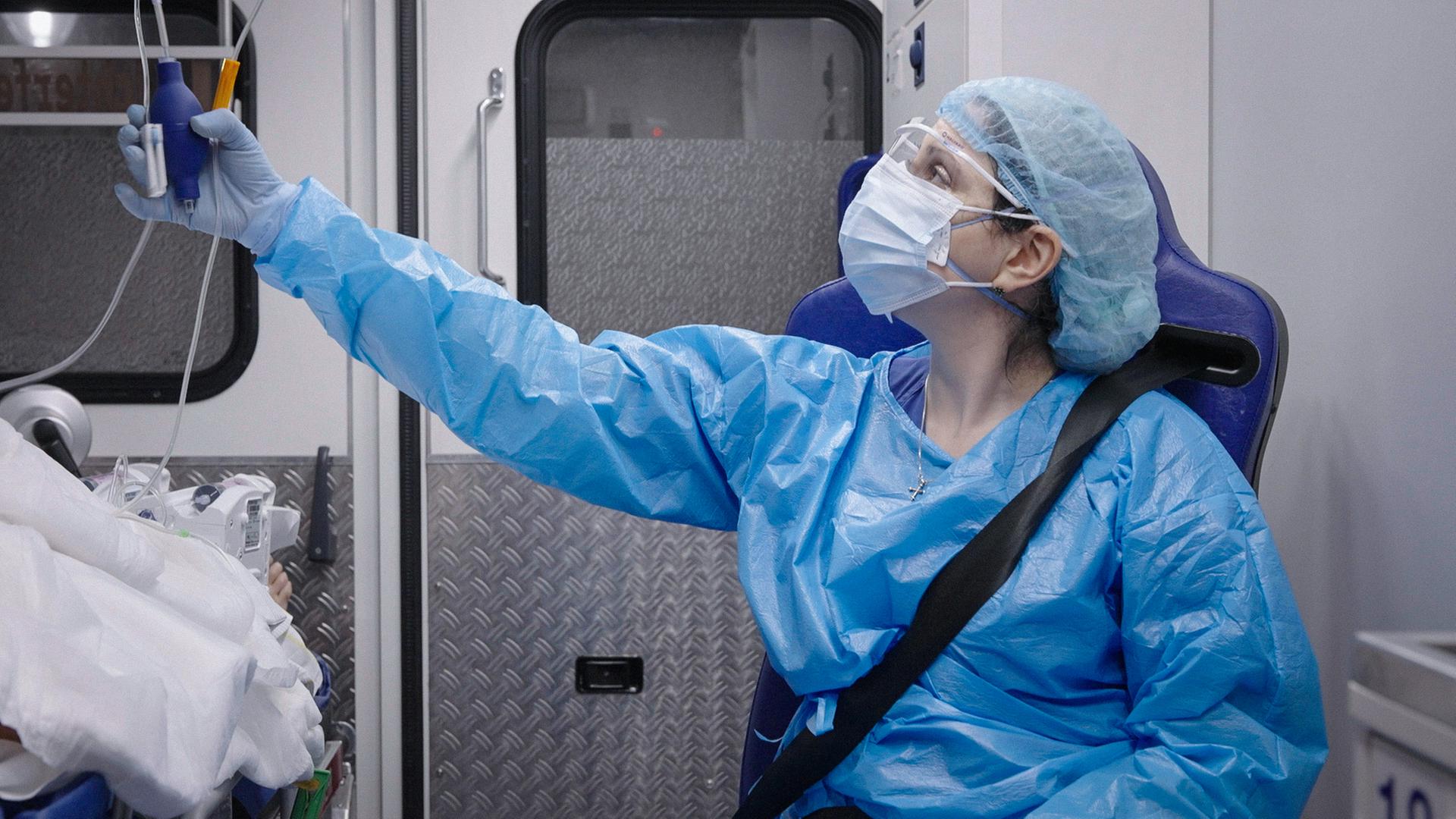 Eine Frau in Schutzmaske und Schutzkleidung im Krankenwagen
