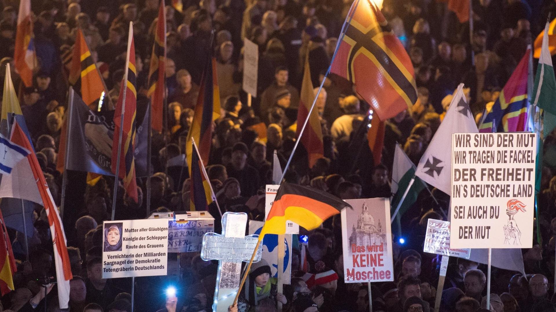 Pegida-Anhänger halten Fahnen und Plakate hoch. Pegida-Anhänger halten Fahnen und Plakate hoch.