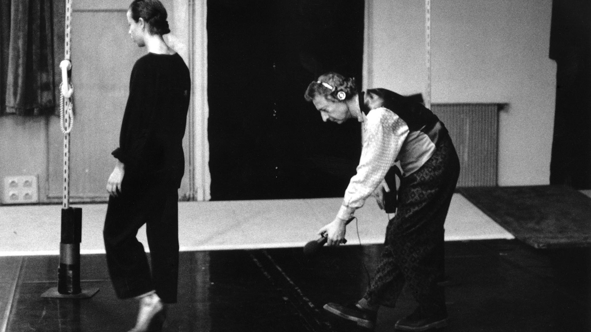 Luc Ferrari steht mit einem Mikrofon gebeugt und einem Kopfhörer auf dem Kopf vor einer jungen Frau und nimmt die Geräusche ihrer Schuhe auf. Luc Ferrari steht mit einem Mikrofon gebeugt und einem Kopfhörer auf dem Kopf vor einer jungen Frau und nimmt die Geräusche ihrer Schuhe auf.