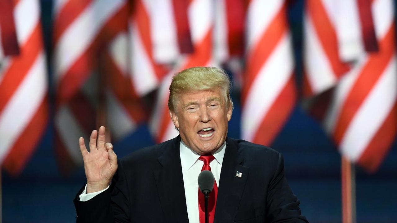Trump steht vor einer Reihe US-amerikanischer Flaggen an einem Rednerpult Trump steht vor einer Reihe US-amerikanischer Flaggen an einem Rednerpult