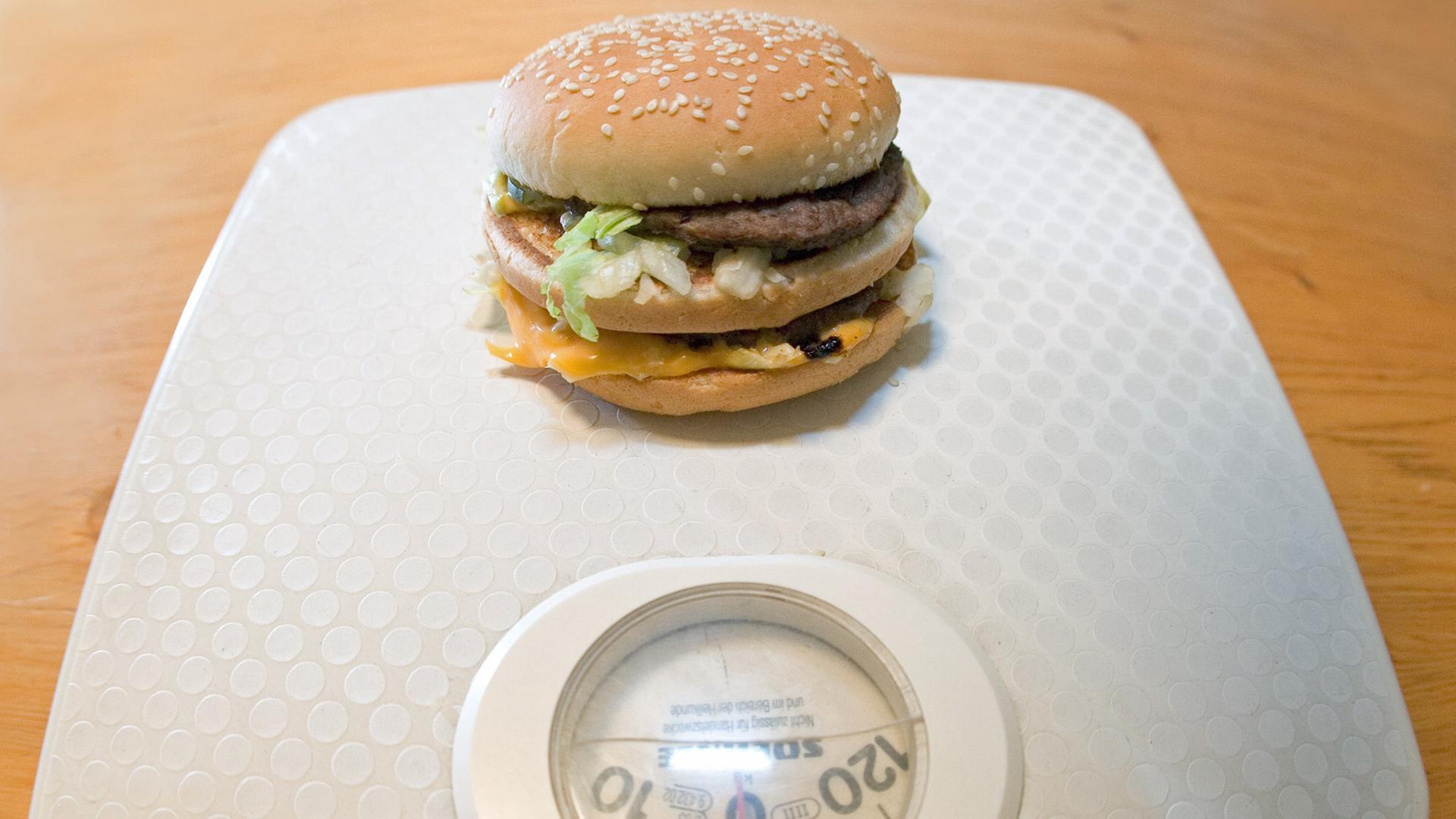Ein Big Mac auf einer Personenwaage / Symbolbild Übergewicht