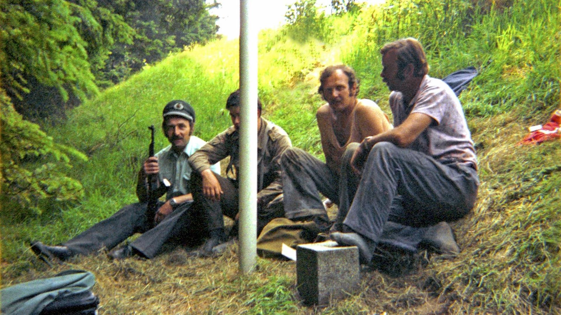 Ein bayerischer Grenzpolizist neben seinem DDR-Kollegen mit dessen Dienstmütze und Kalaschnikow. Daneben zwei ostdeutsche Bauarbeiter. Sommer 1981 an der deutsch-deutschen Grenze zwischen Hof und Plauen. Ein bayerischer Grenzpolizist neben seinem DDR-Kollegen mit dessen Dienstmütze und Kalaschnikow. Daneben zwei ostdeutsche Bauarbeiter. Sommer 1981 an der deutsch-deutschen Grenze zwischen Hof und Plauen.