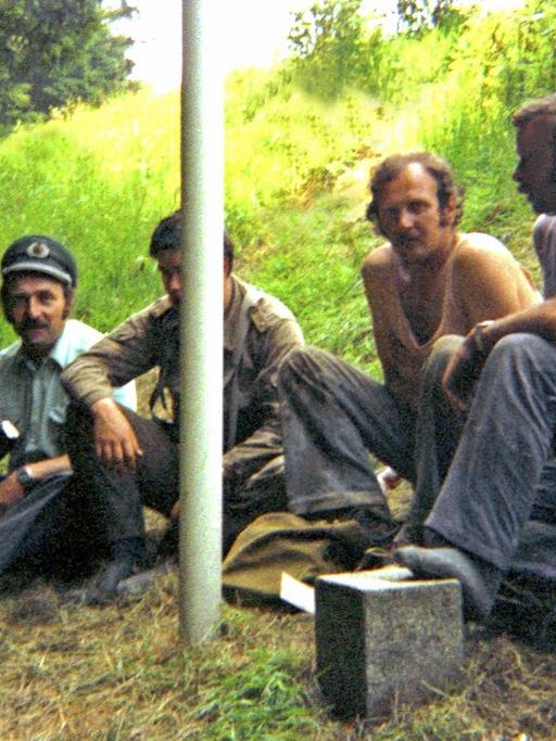 Ein bayerischer Grenzpolizist neben seinem DDR-Kollegen mit dessen Dienstmütze und Kalaschnikow. Daneben zwei ostdeutsche Bauarbeiter. Sommer 1981 an der deutsch-deutschen Grenze zwischen Hof und Plauen.
