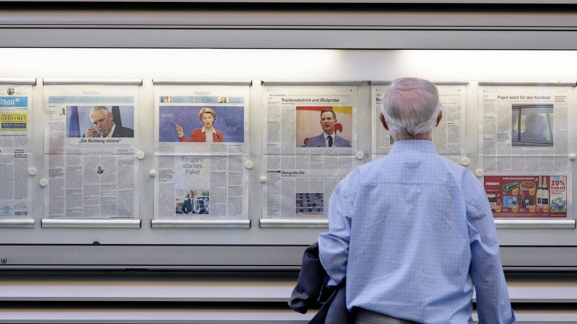 Ein Mann steht vor einer Zeitung in einem Schaukasten Ein Mann steht vor einer Zeitung in einem Schaukasten