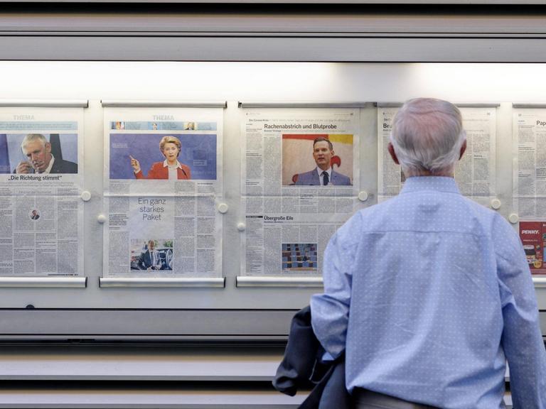 Ein Mann steht vor einer Zeitung in einem Schaukasten