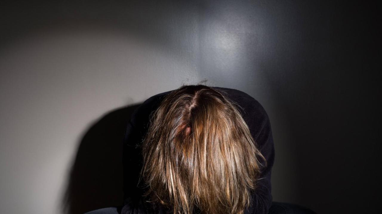 Eine Frau sitz in einem dunklen Zimmer, den Kopf gesenkt
