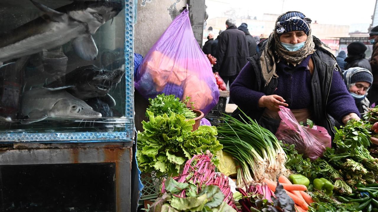 Eine Marktfrau mit Covid-Maske verkauft Gemüse und Fisch auf dem zentralen Markt in Tiflis, Georgien. Dezember 2020. Eine Marktfrau mit Covid-Maske verkauft Gemüse und Fisch auf dem zentralen Markt in Tiflis, Georgien. Dezember 2020.