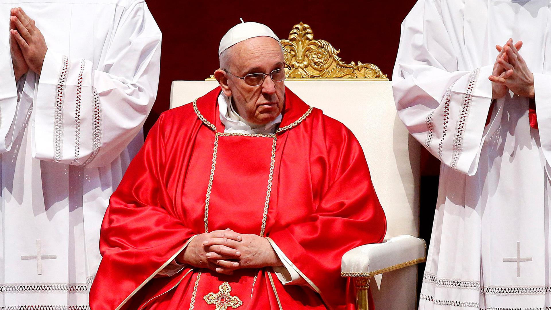 Papst Franziskus sitzt im roten Gewand auf einem weißen Stuhl, rechts und links neben ihm zwei Messdiener in weißen Gewändern mit gefalteten Händen Papst Franziskus sitzt im roten Gewand auf einem weißen Stuhl, rechts und links neben ihm zwei Messdiener in weißen Gewändern mit gefalteten Händen