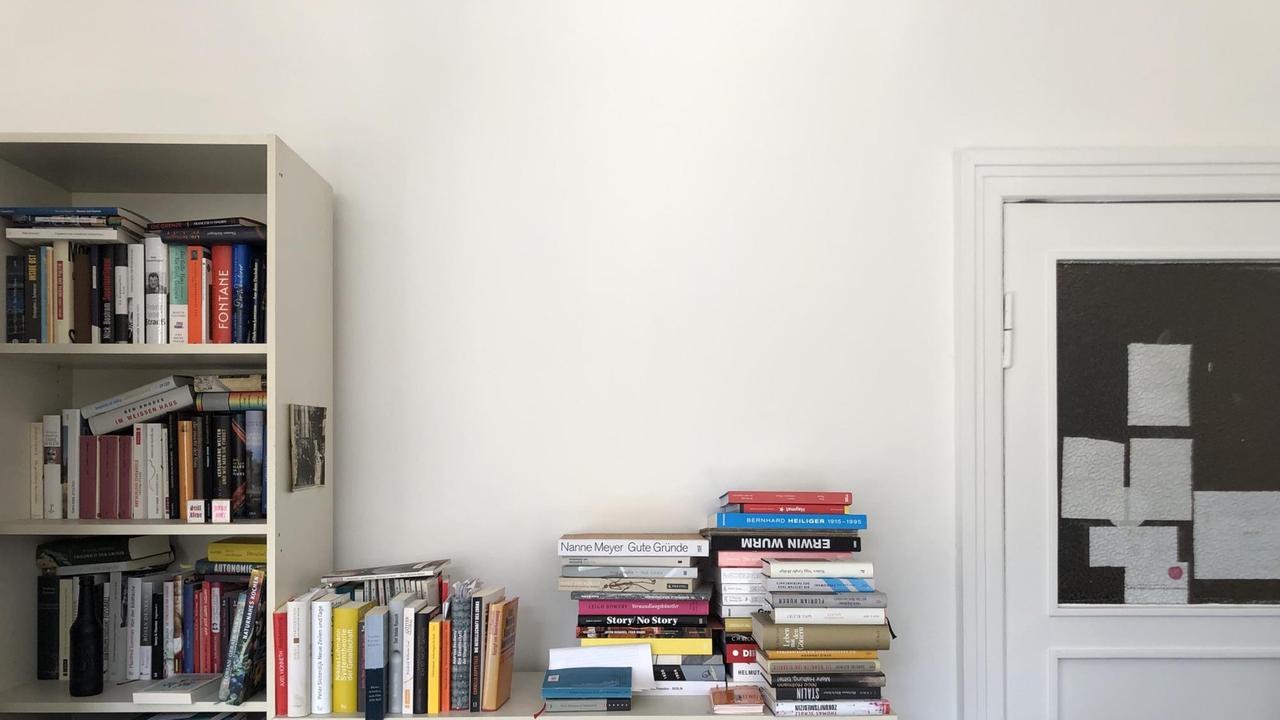 Eine weiße Wand in einem Büro. Links steht ein Regal mit Büchern. 