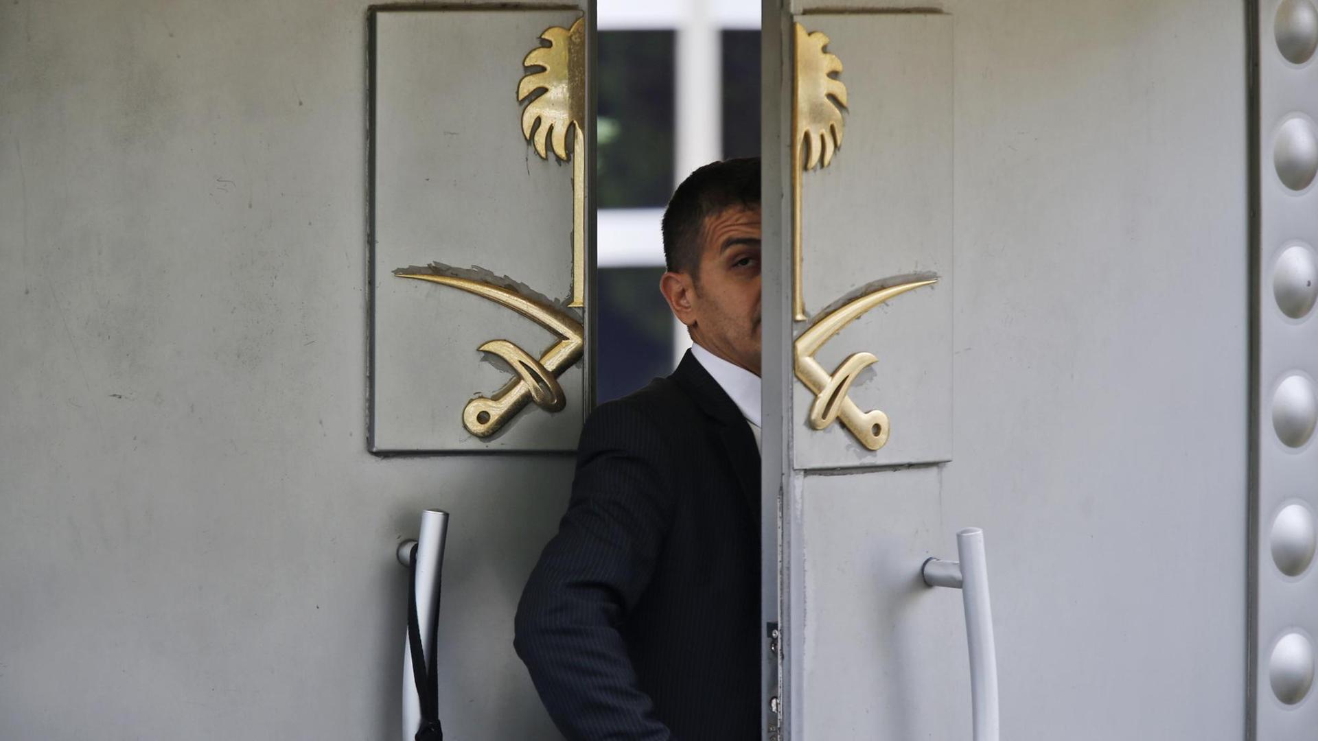 Der Mann steht in dem Eingang und wird halb von einer der beiden Flügeltüren verdeckt. Auf der Tür prangen in gold zwei gekreuzte Säbel vor einer Palme. Der Mann steht in dem Eingang und wird halb von einer der beiden Flügeltüren verdeckt. Auf der Tür prangen in gold zwei gekreuzte Säbel vor einer Palme.