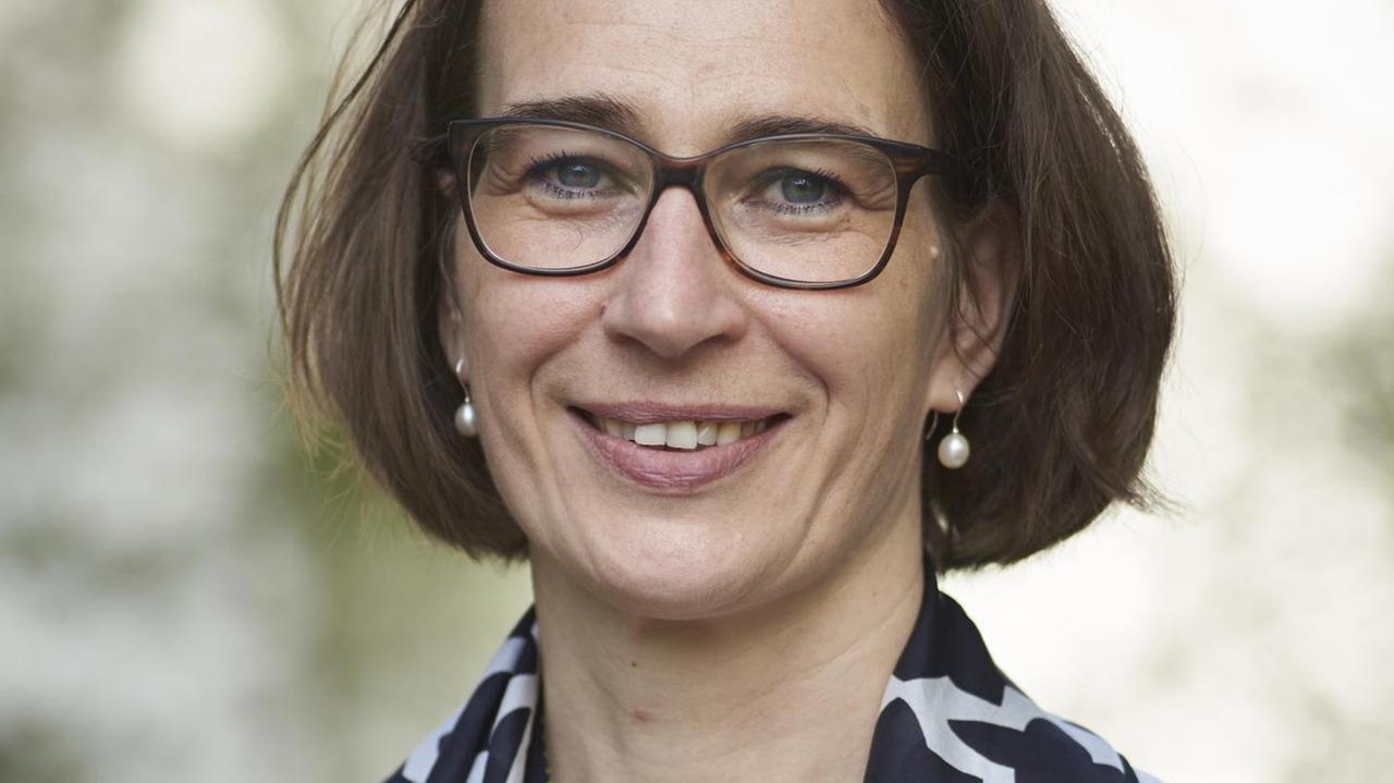 Die Politologin Sandra Seubert, mit Brille, in einer weißen Bluse mit schwarz gemustertem Seidentuch über den Schultern, lächelt in die Kamera