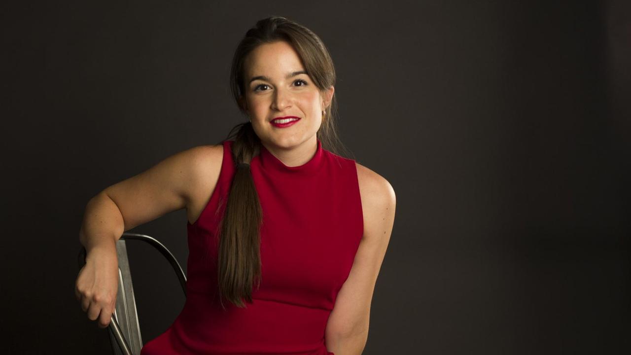 Eine junge Frau im roten Kleid und langem, dunklen Haar sitzt aufrecht auf einem Stuhl und lächelt. Eine junge Frau im roten Kleid und langem, dunklen Haar sitzt aufrecht auf einem Stuhl und lächelt.