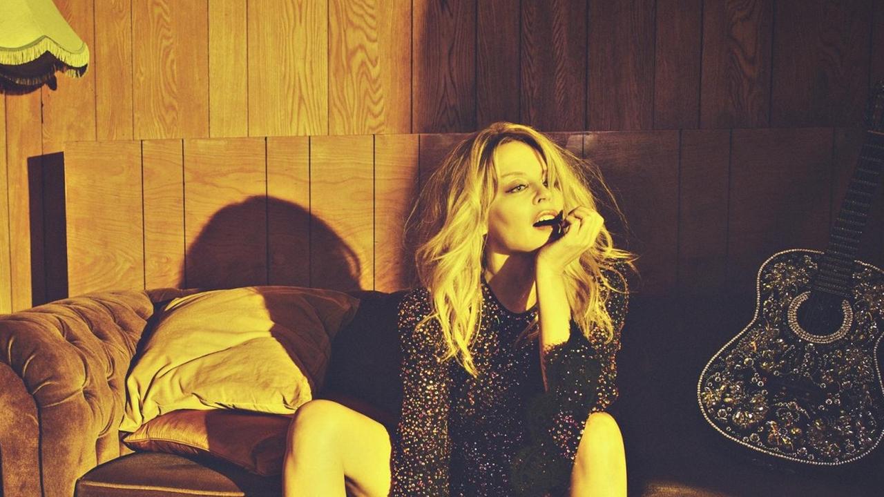 Kylie Minogue sitzt auf einem alten Sofa und rechts von liegt eine typische Country Gitarre Kylie Minogue sitzt auf einem alten Sofa und rechts von liegt eine typische Country Gitarre