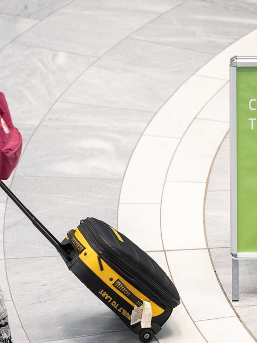03.08.2020 - Reisende mit Rollkoffer und Sonnenhut, daneben ein Wegweiser zum "Corona-Testzentrum" am Stuttgarter Flughafen